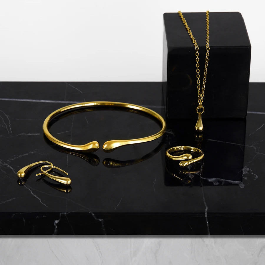 Conjunto de joias em formato de gota, composto por quatro peças em ouro ou prata: brincos, colar, pulseira e anel.