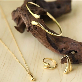 Conjunto de joias em formato de gota, composto por quatro peças em ouro ou prata: brincos, colar, pulseira e anel.